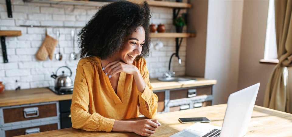 lady sitting in kitchen smiling at laptop