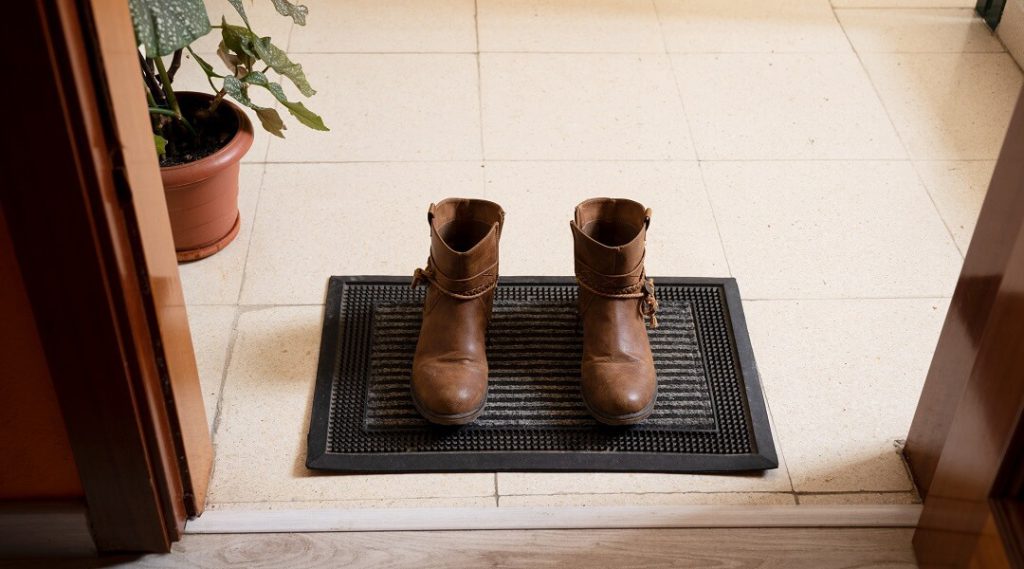 A rugged floor mat placed at the front door with a pair of leather boots resting atop.