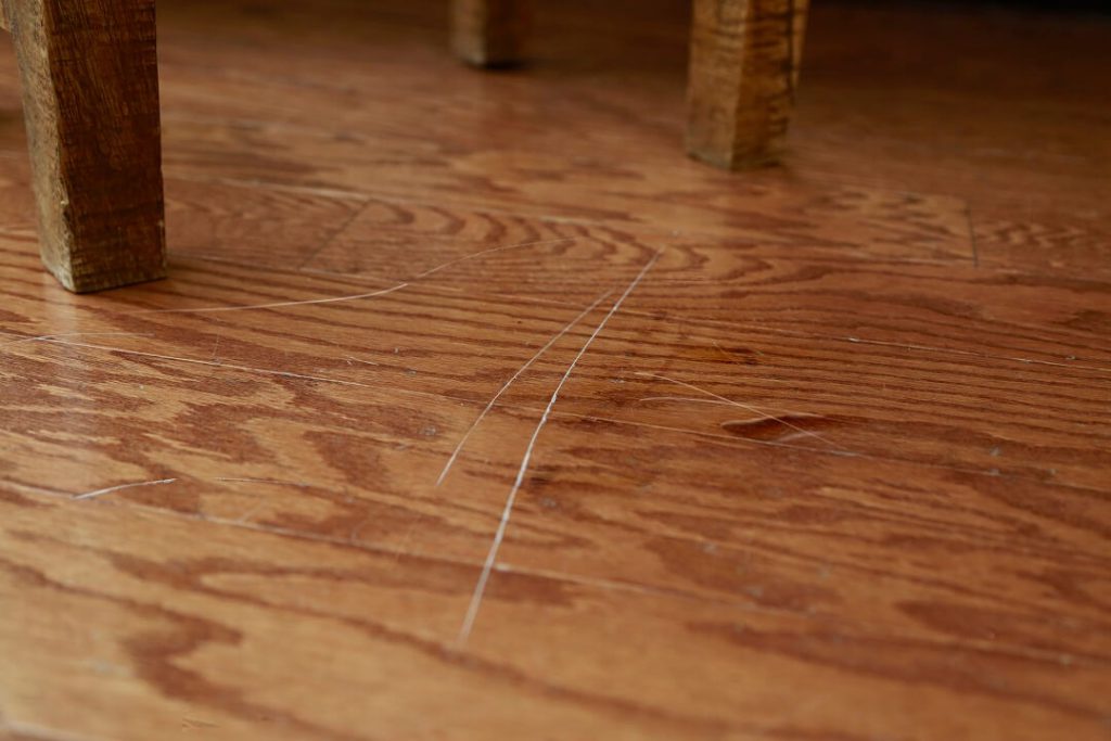 Closeup of a hardwood floor with deep scratches caused by the chair legs seen in the photo.