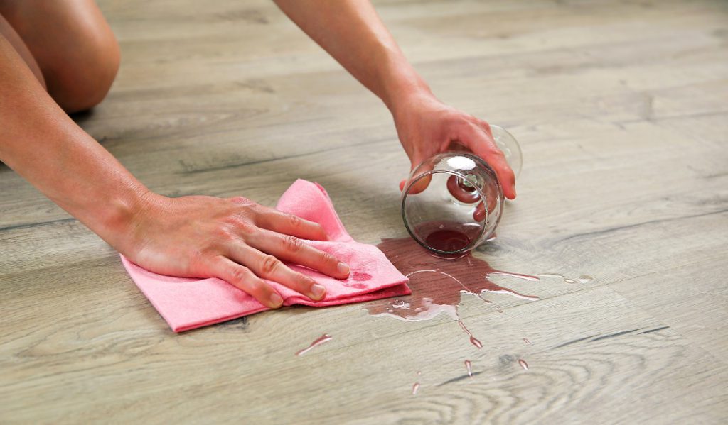 Person cleaning spilled red wine off of laminate wood kitchen flooring.